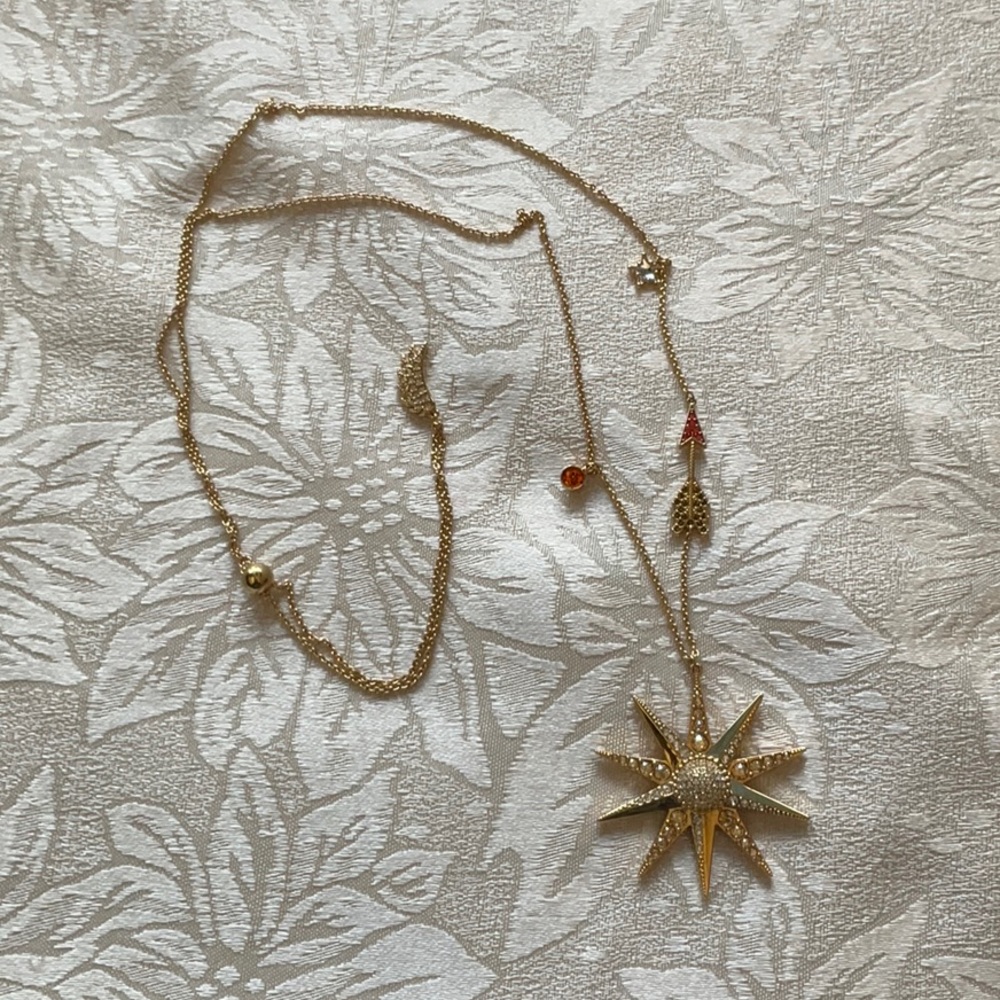 Swarovski gold tone sun/star necklace with arrow, wing, star, and circle charms.